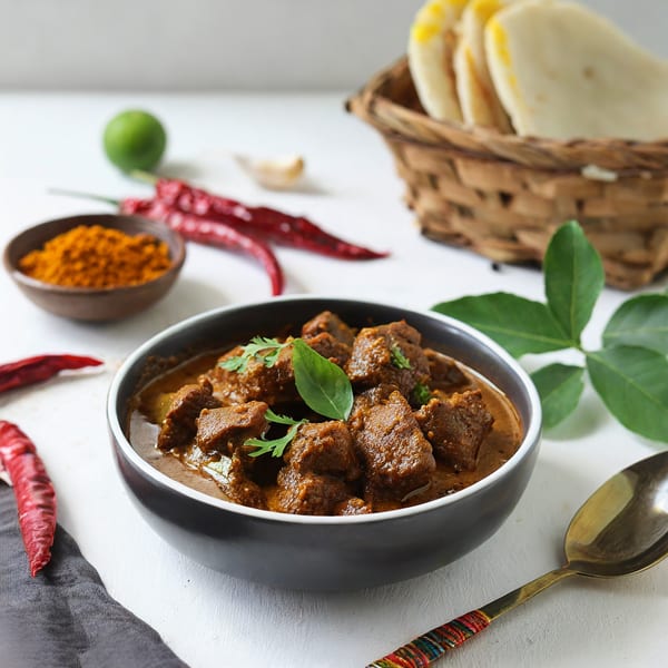 Indian lamb curry with naan bread, spices, and lime on a white table.