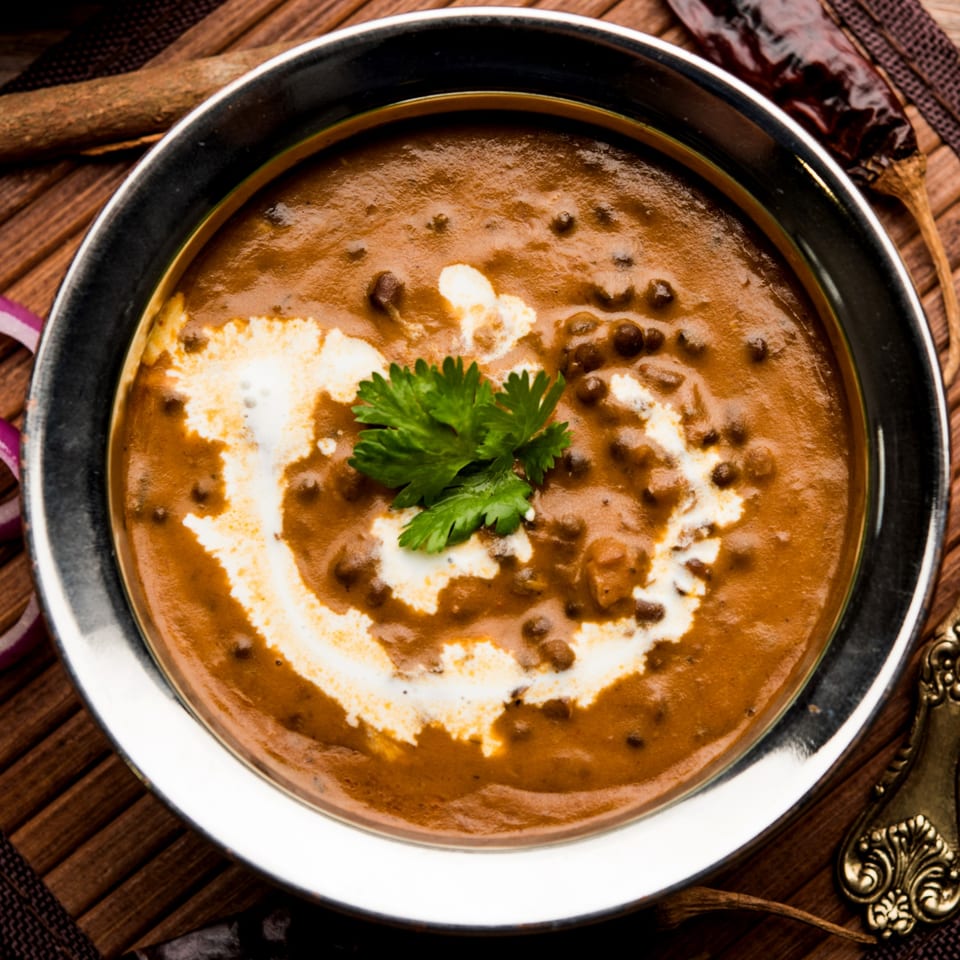 A bowl of Indian dal makhani, garnished with cream swirls and fresh cilantro, on a wooden mat.