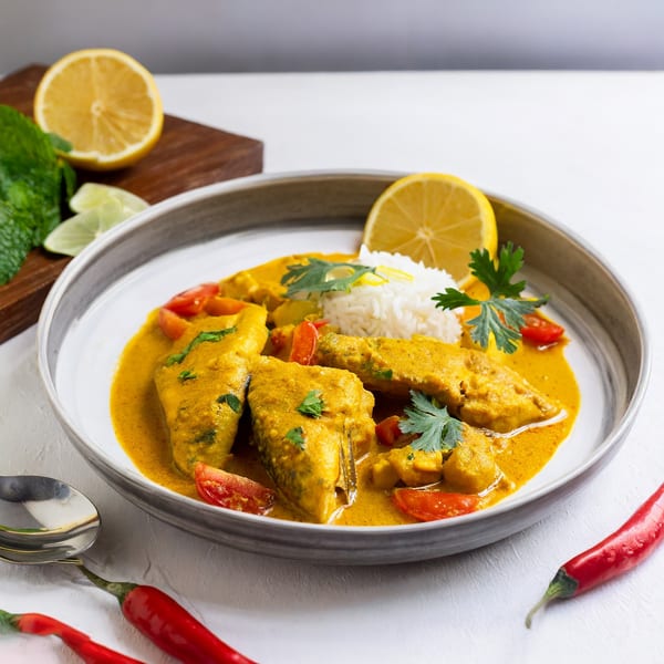 Indian fish curry with rice, tomatoes, and cilantro, garnished with lemon and red chilies.