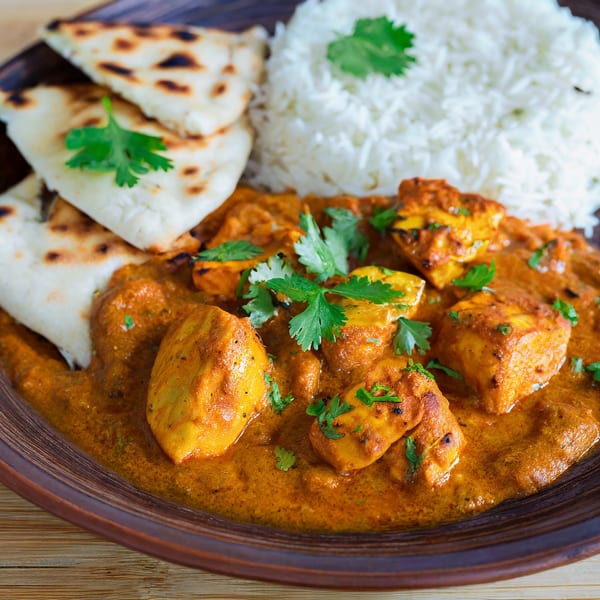 Indian butter chicken with rice and naan bread, garnished with fresh cilantro on a brown plate.